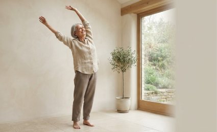 An older person reaching upward in a bright, plain room.